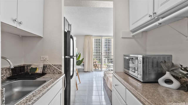 kitchen with white cabinets, light tile patterned floors, fridge, and sink