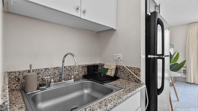 kitchen featuring light stone countertops, sink, light tile patterned floors, black fridge, and white cabinets