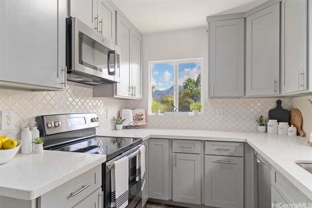 kitchen featuring appliances with stainless steel finishes, light stone countertops, decorative backsplash, and gray cabinetry