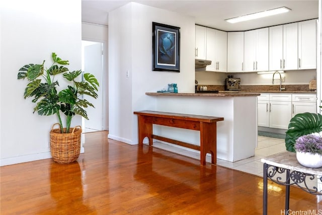 kitchen with dark stone counters, white cabinets, sink, light hardwood / wood-style floors, and kitchen peninsula