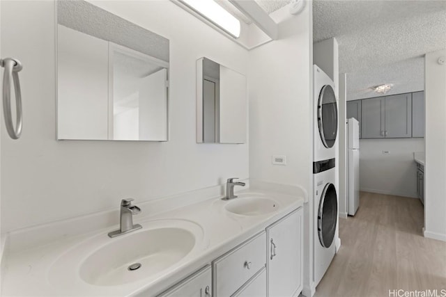 bathroom with hardwood / wood-style flooring, vanity, stacked washing maching and dryer, and a textured ceiling