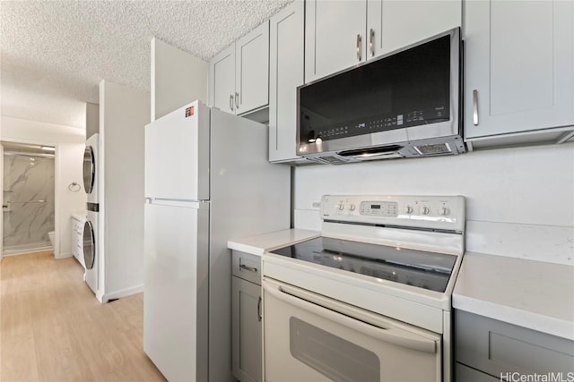 kitchen featuring light wood-type flooring, a textured ceiling, white appliances, and stacked washer and dryer