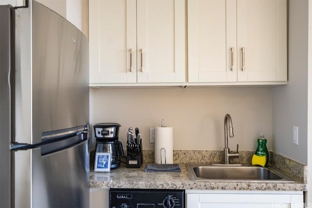 kitchen with stainless steel refrigerator, light stone countertops, sink, black dishwasher, and white cabinets