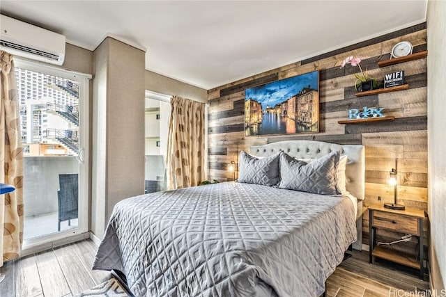 bedroom featuring a wall unit AC, access to exterior, wood walls, and light hardwood / wood-style floors