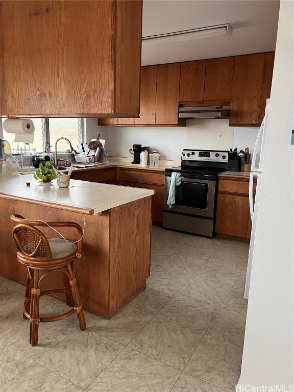 kitchen featuring stainless steel electric range oven, kitchen peninsula, a breakfast bar, and sink