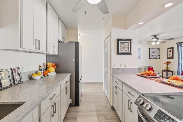 kitchen with appliances with stainless steel finishes, white cabinetry, light hardwood / wood-style flooring, ceiling fan, and light stone counters