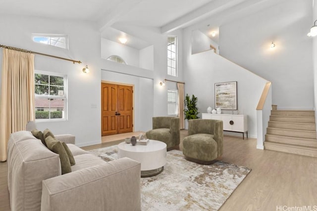 living room with a towering ceiling, light hardwood / wood-style flooring, and beamed ceiling