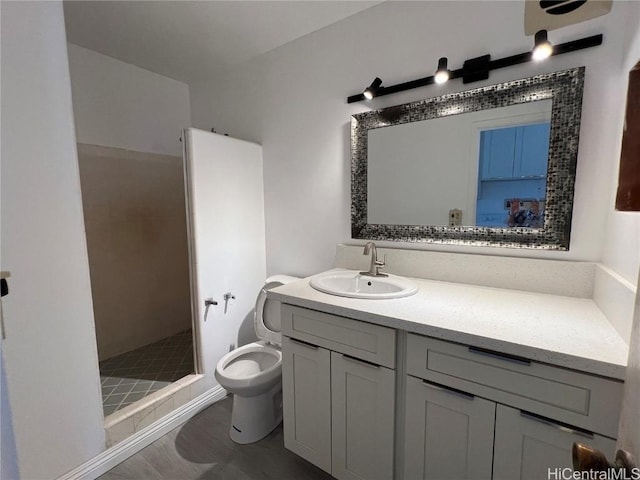 bathroom featuring vanity, toilet, wood-type flooring, and tiled shower