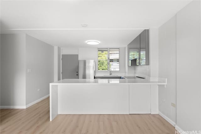 kitchen with stainless steel refrigerator, sink, kitchen peninsula, and light wood-type flooring