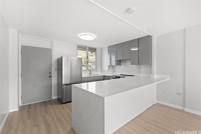 kitchen with sink, gray cabinets, light hardwood / wood-style floors, kitchen peninsula, and stainless steel appliances