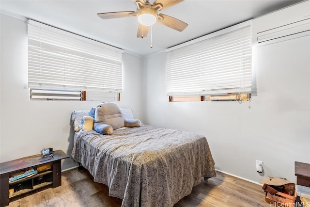 bedroom featuring a ceiling fan, an AC wall unit, and wood finished floors