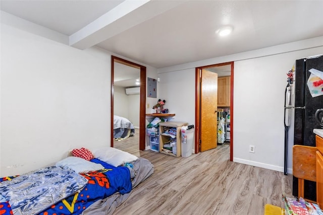 bedroom with light wood finished floors, a wall mounted air conditioner, freestanding refrigerator, and baseboards