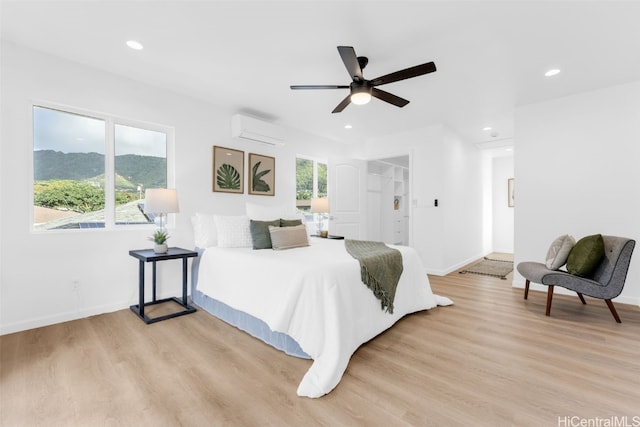 bedroom with a wall mounted AC, ceiling fan, a spacious closet, multiple windows, and light hardwood / wood-style floors