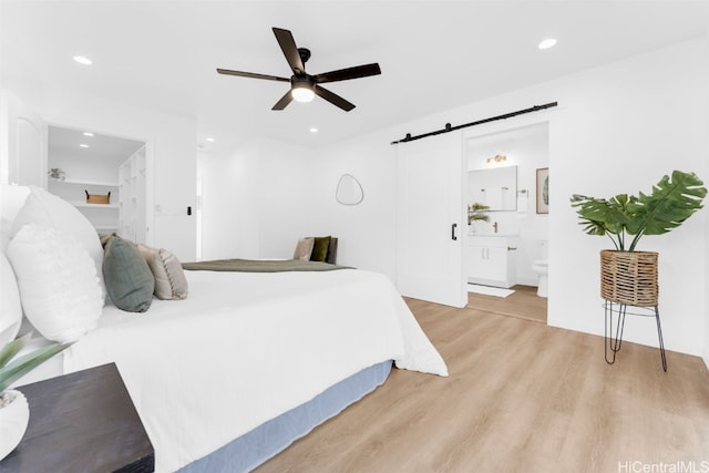 bedroom featuring ceiling fan, a barn door, light hardwood / wood-style floors, and ensuite bath