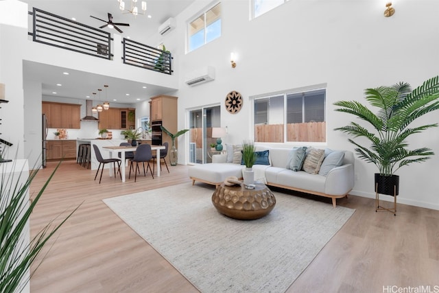 living room featuring baseboards, a ceiling fan, light wood-type flooring, and a wall unit AC