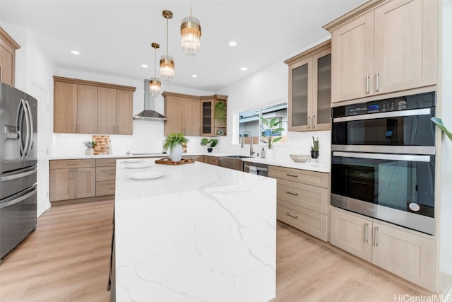 kitchen with hanging light fixtures, wall chimney exhaust hood, light hardwood / wood-style floors, appliances with stainless steel finishes, and a kitchen island