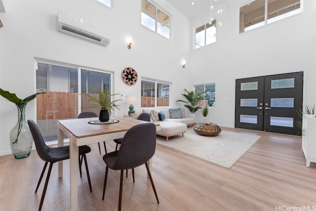 dining space with an AC wall unit, french doors, light hardwood / wood-style floors, and a high ceiling