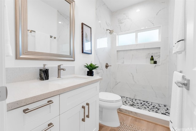 bathroom with toilet, hardwood / wood-style floors, vanity, and tiled shower