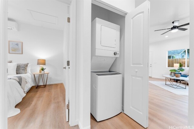 laundry area featuring a wall mounted air conditioner, stacked washing maching and dryer, light hardwood / wood-style flooring, and ceiling fan