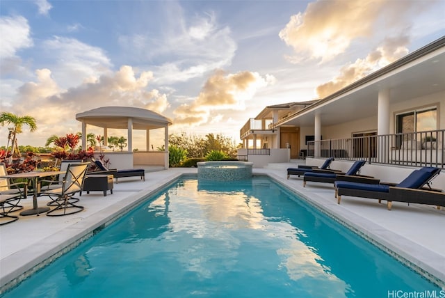 pool at dusk with a patio area and an in ground hot tub