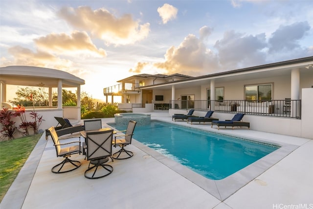 pool at dusk featuring a patio area and an in ground hot tub