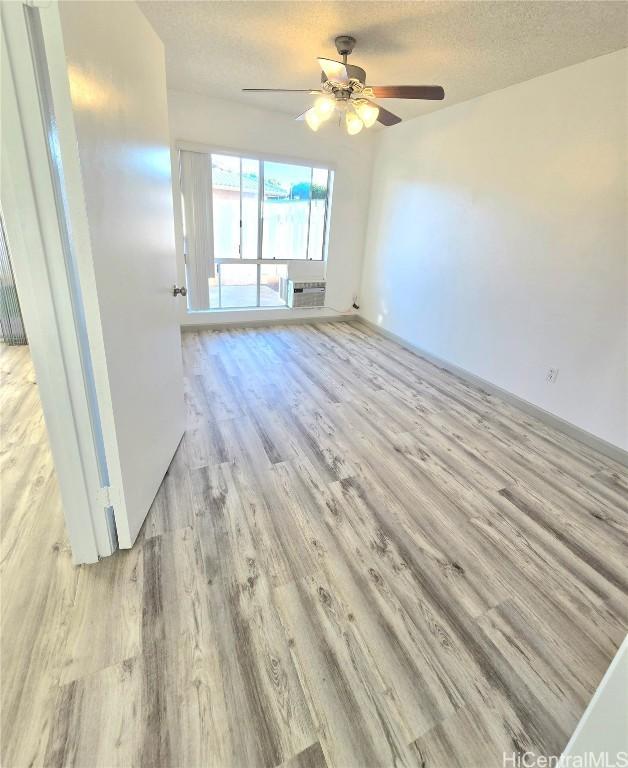 spare room with ceiling fan, light hardwood / wood-style floors, an AC wall unit, and a textured ceiling