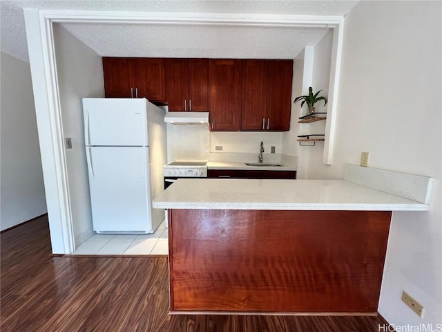 kitchen featuring white appliances, wood-type flooring, kitchen peninsula, and sink