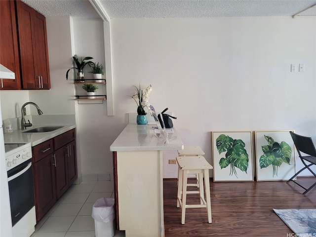 kitchen with white electric stove, a textured ceiling, a sink, light countertops, and a breakfast bar