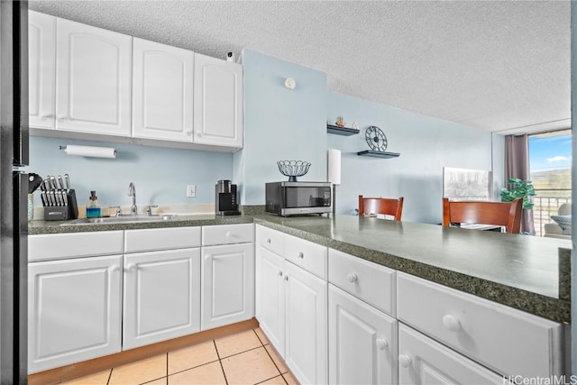 kitchen featuring white cabinets, sink, light tile patterned floors, and a textured ceiling