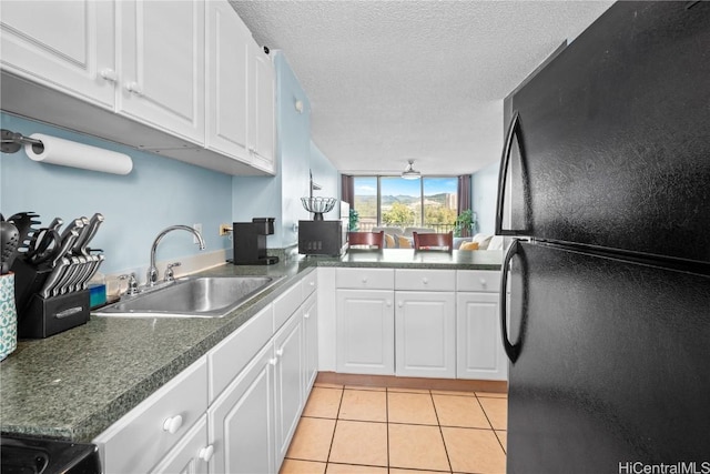 kitchen with sink, white cabinetry, black fridge, and light tile patterned flooring