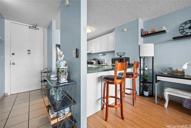 kitchen featuring a breakfast bar, light tile patterned floors, a textured ceiling, and white cabinetry