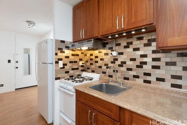 kitchen with white appliances, sink, light wood-type flooring, tasteful backsplash, and extractor fan