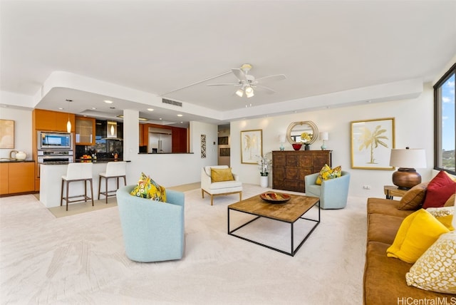 living room featuring a tray ceiling, ceiling fan, and light colored carpet