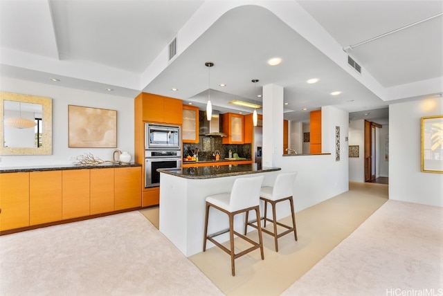 kitchen with stainless steel appliances, wall chimney range hood, tasteful backsplash, dark stone countertops, and pendant lighting