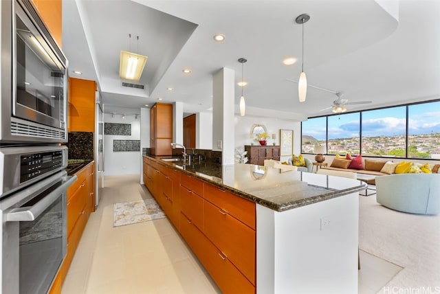 kitchen featuring kitchen peninsula, stainless steel appliances, ceiling fan, dark stone countertops, and hanging light fixtures