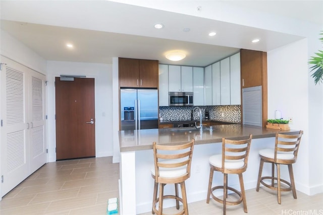 kitchen featuring kitchen peninsula, stainless steel appliances, a breakfast bar area, and tasteful backsplash