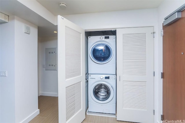 laundry area with electric panel, stacked washing maching and dryer, and light hardwood / wood-style flooring