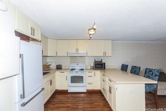 kitchen with white appliances, kitchen peninsula, a textured ceiling, dark hardwood / wood-style floors, and a breakfast bar