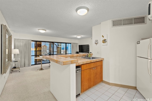 kitchen featuring dishwasher, white refrigerator, sink, tile counters, and kitchen peninsula