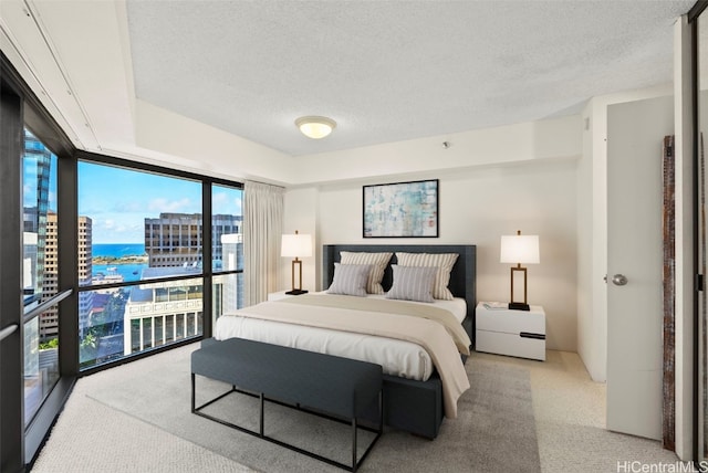 bedroom with a textured ceiling, light colored carpet, a wall of windows, and a water view