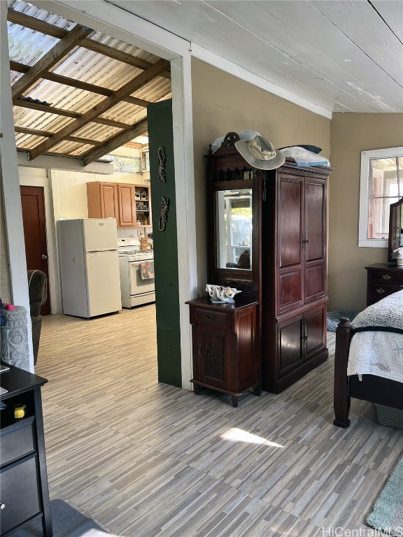 bedroom with vaulted ceiling with beams, white fridge, and light hardwood / wood-style floors