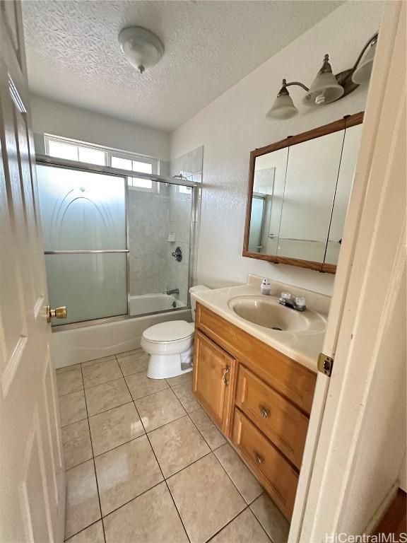 full bathroom with tile patterned floors, a textured ceiling, toilet, shower / bath combination with glass door, and vanity