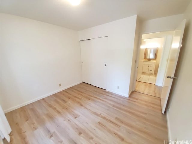 unfurnished bedroom with a closet, connected bathroom, and light hardwood / wood-style flooring