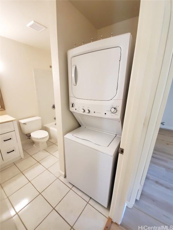 clothes washing area with light tile patterned floors and stacked washer and clothes dryer