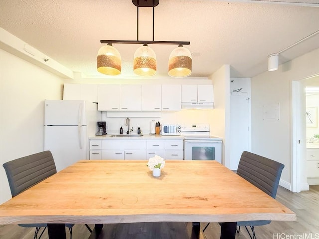 kitchen with pendant lighting, white appliances, sink, light hardwood / wood-style floors, and white cabinetry