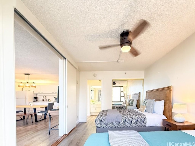 bedroom featuring ceiling fan, light hardwood / wood-style flooring, white fridge, and a textured ceiling