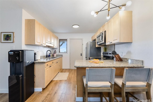 kitchen with sink, light brown cabinetry, appliances with stainless steel finishes, light hardwood / wood-style floors, and kitchen peninsula