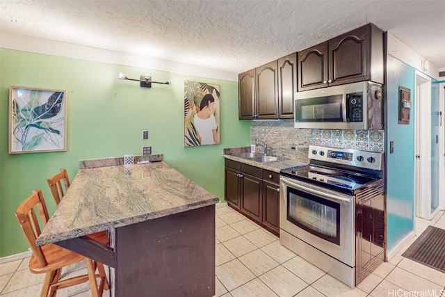 kitchen with light tile patterned flooring, dark brown cabinetry, a breakfast bar area, a textured ceiling, and appliances with stainless steel finishes