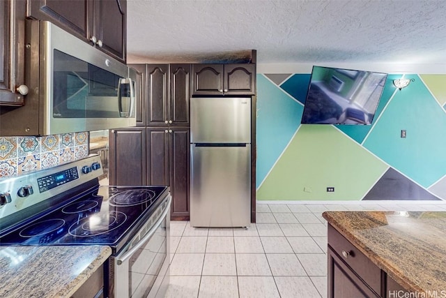 kitchen with appliances with stainless steel finishes, light stone counters, dark brown cabinetry, a textured ceiling, and light tile patterned flooring