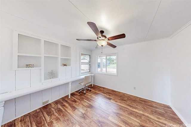 unfurnished office featuring a ceiling fan, built in desk, and wood finished floors